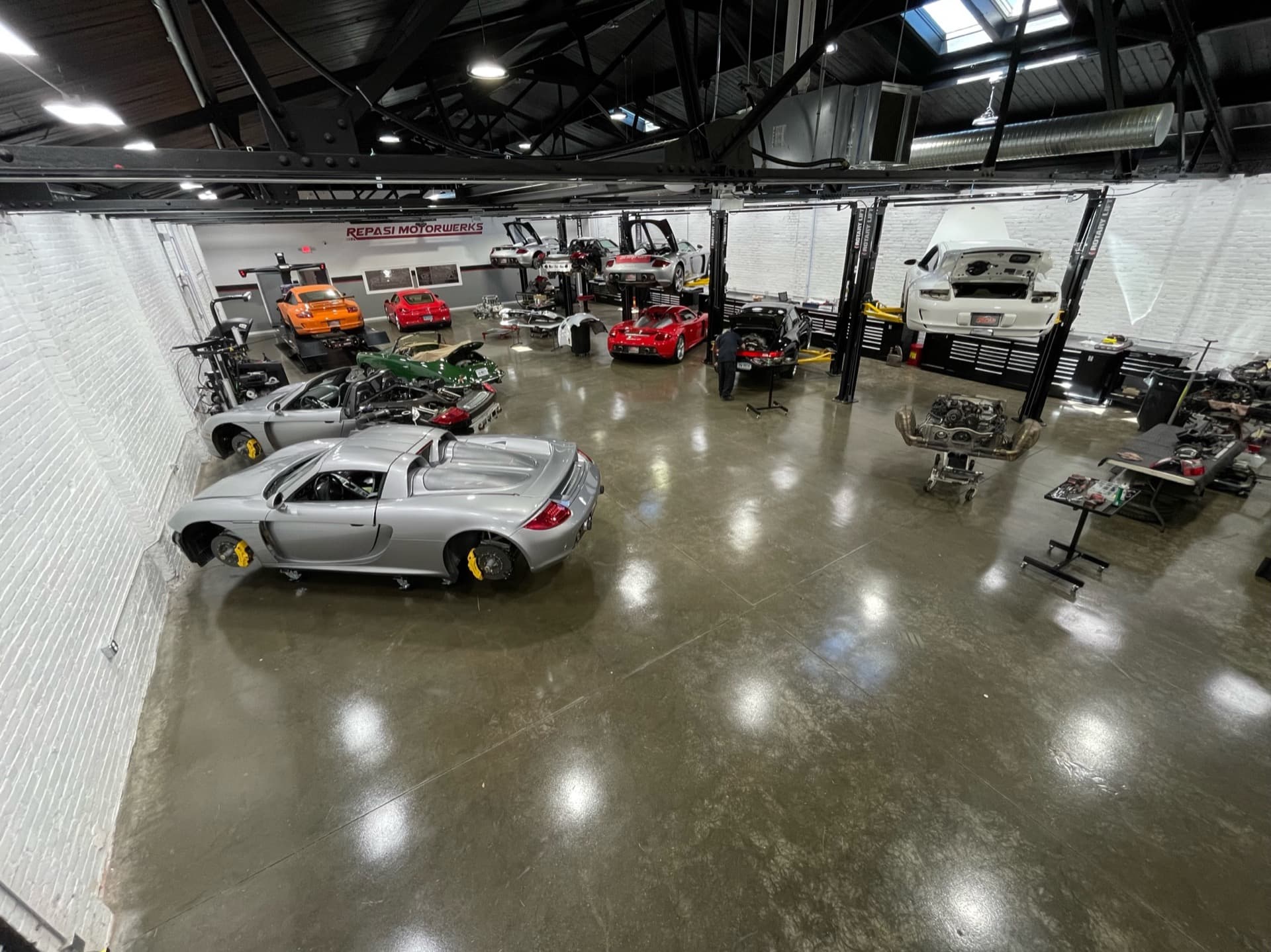 Wide aerial view of a silver Porsche Carrera GT and orange GT3 RS inside the Repasi Motorwerks workshop