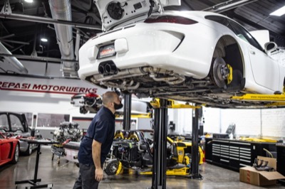 Technician inspecting the underside of a white Porsche 991 GT3 on the lift